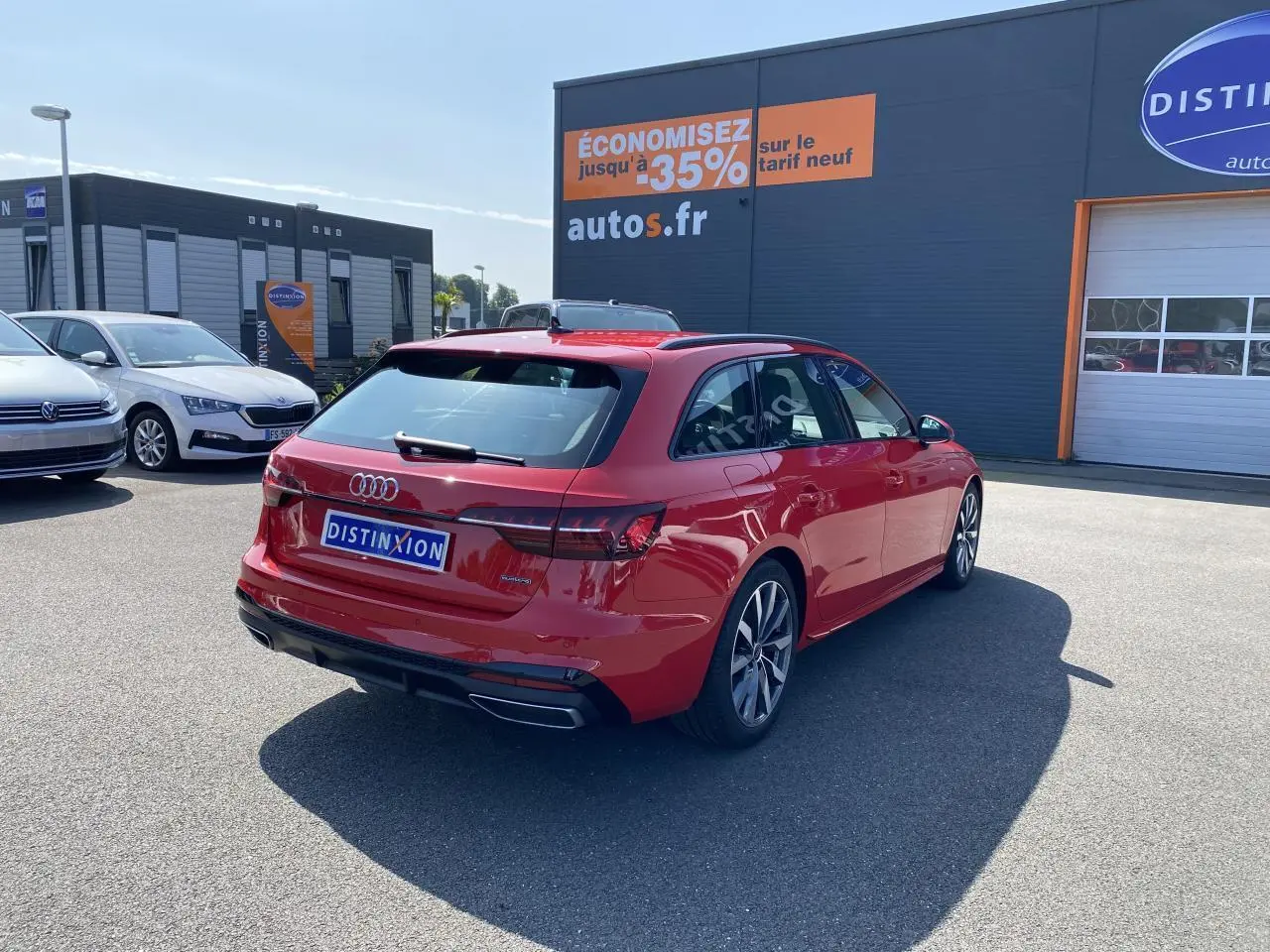 Audi A4 Avant S line rouge Tango vue 3/4 arrière droit sur parking devant un bâtiment commercial