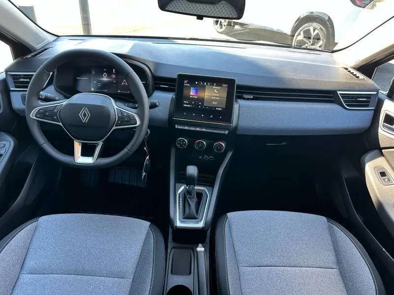 Intérieur avant de la Renault Clio 2025 avec tableau de bord gris, volant multifonction et écran tactile central.