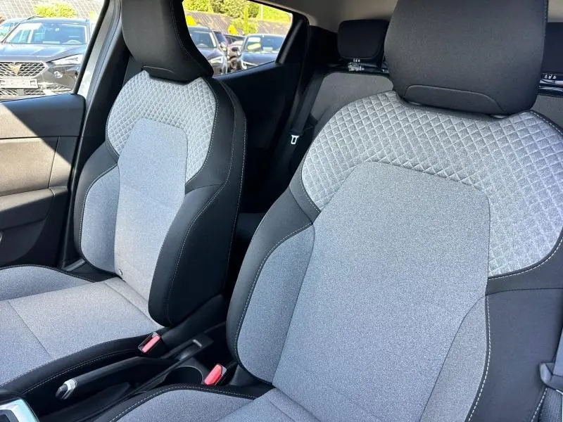 Gros plan sur les sièges avant gris clair et noir de la Renault Clio 2025, avec tissu à motif 3D et ceintures visibles.