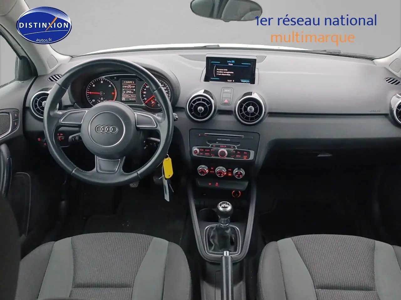 Vue intérieure frontale de l'Audi A1 blanche de 2015, avec tableau de bord noir et volant cuir multifonction.