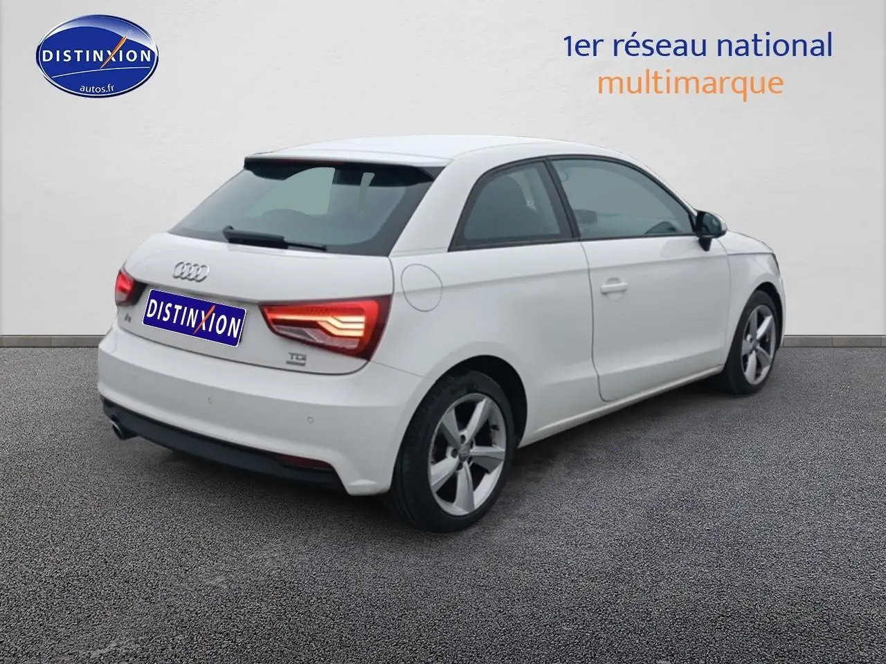 Audi A1 blanc vue 3/4 arrière droit, feux arrière allumés et jantes alliage cinq branches.