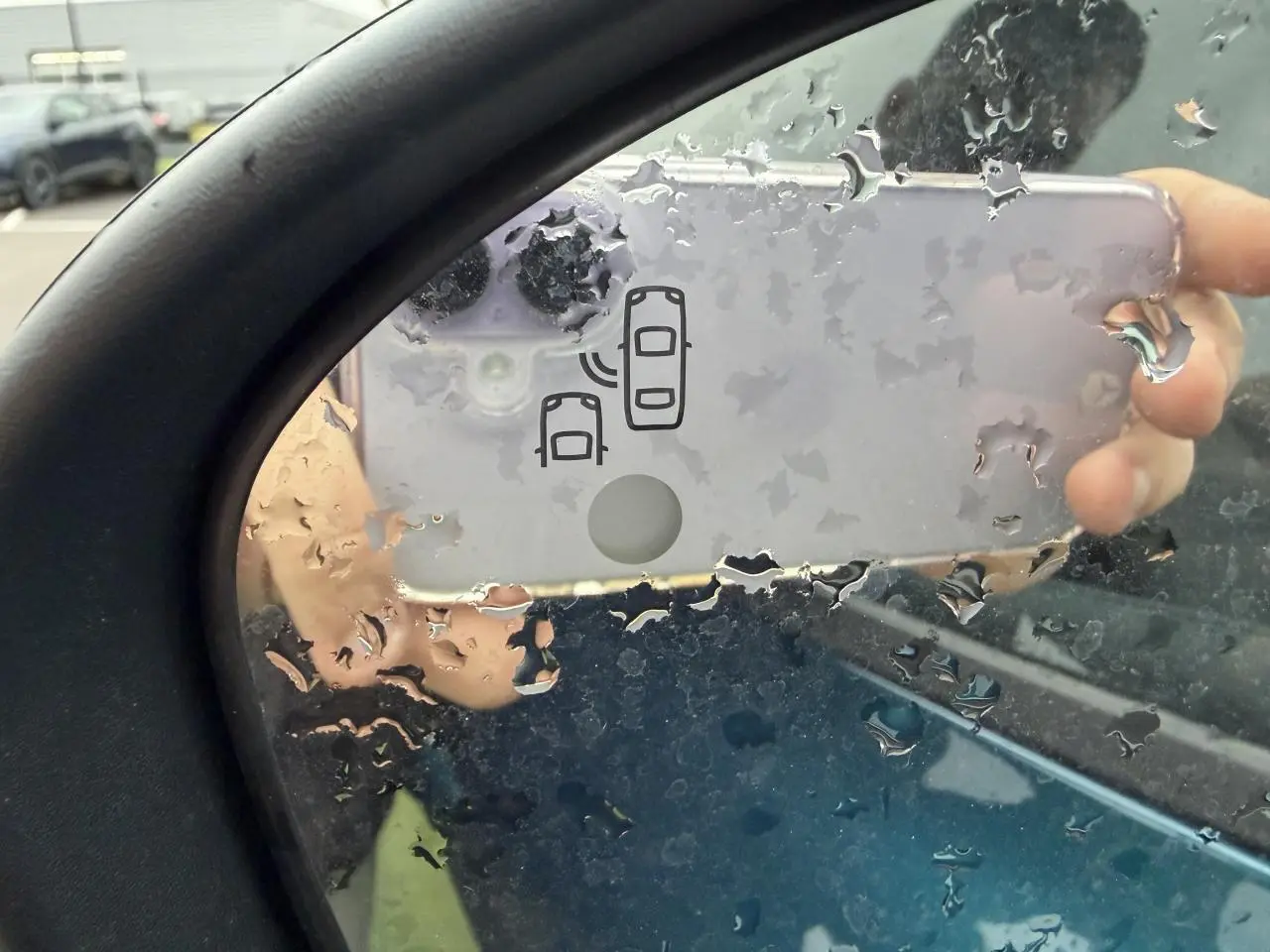 Rétroviseur gauche d’un Renault Arkana bleu Zanzibar, avec icône d’alerte d’angle mort visible sous la pluie.