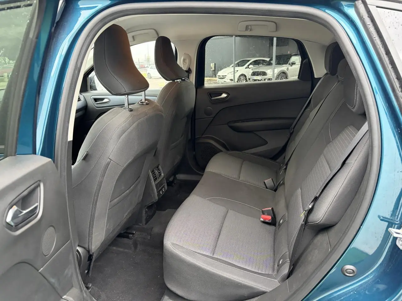 Vue intérieure arrière côté gauche du Renault Arkana bleu Zanzibar, montrant les sièges arrière en tissu gris et les portes ouvertes.