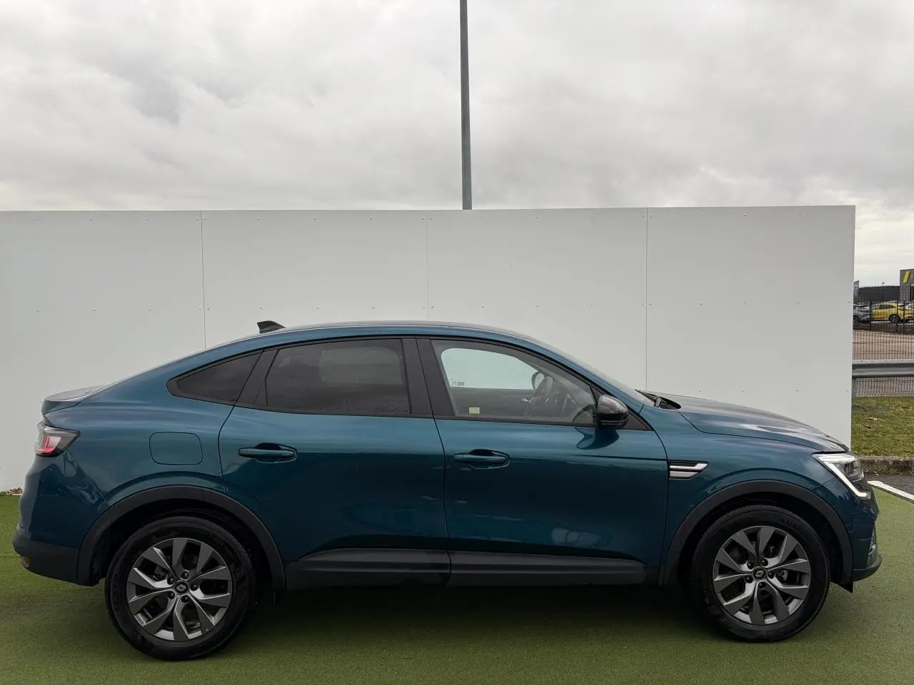 Profil droit d'un Renault Arkana bleu Zanzibar métallisé avec vitres surteintées et jantes alliage grises 17 pouces.