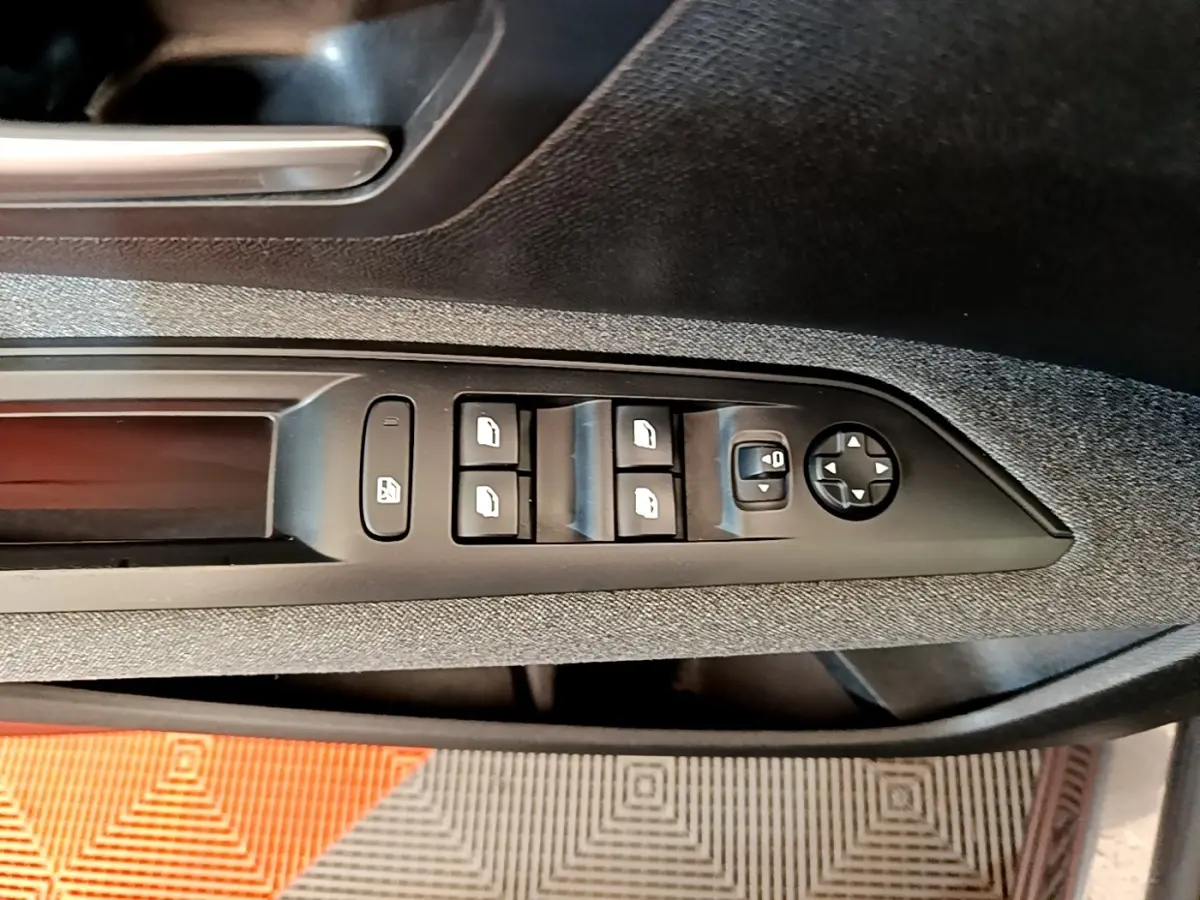 Détail des commandes des vitres électriques et rétroviseurs sur la porte côté conducteur d’un Peugeot 5008 gris clair.