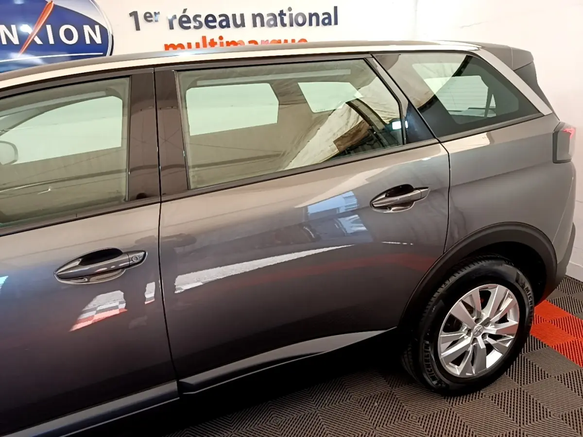Vue côté droit arrière d'un Peugeot 5008 gris clair avec jantes alliage et poignées de porte chromées.