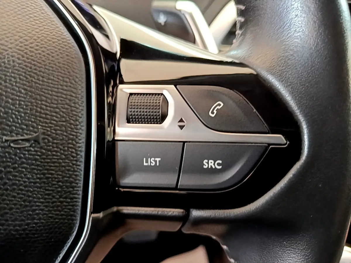 Gros plan sur les commandes gauche du volant cuir noir du Peugeot 5008 gris clair, boutons multifonctions visibles.