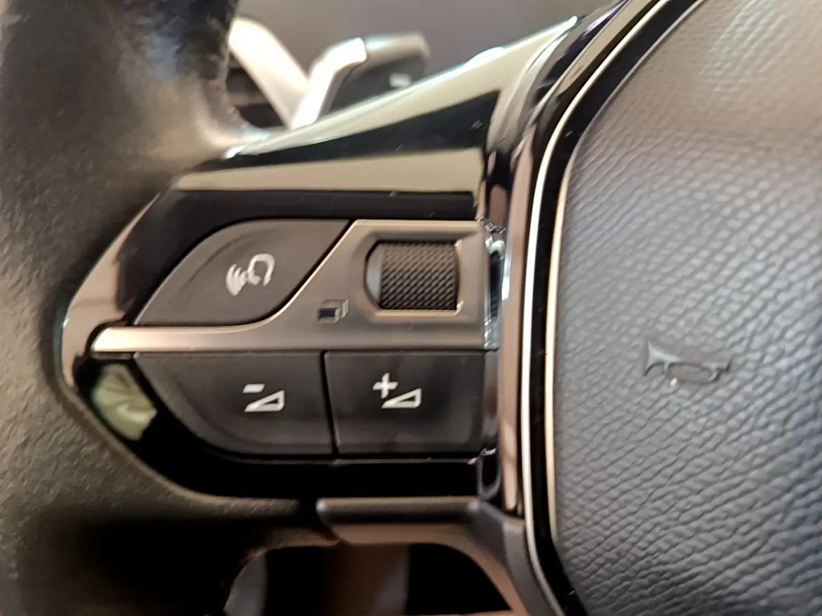Gros plan sur les commandes de volume et appel vocal sur le volant cuir noir du Peugeot 5008 gris clair.