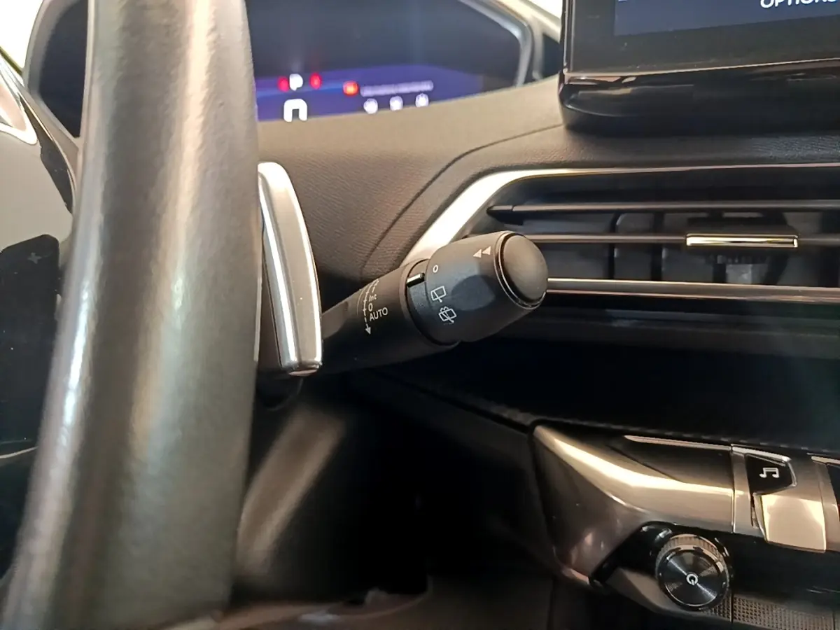 Gros plan sur la commande d’essuie-glace à gauche du volant cuir dans l’habitacle sombre d’un Peugeot 5008 gris clair.