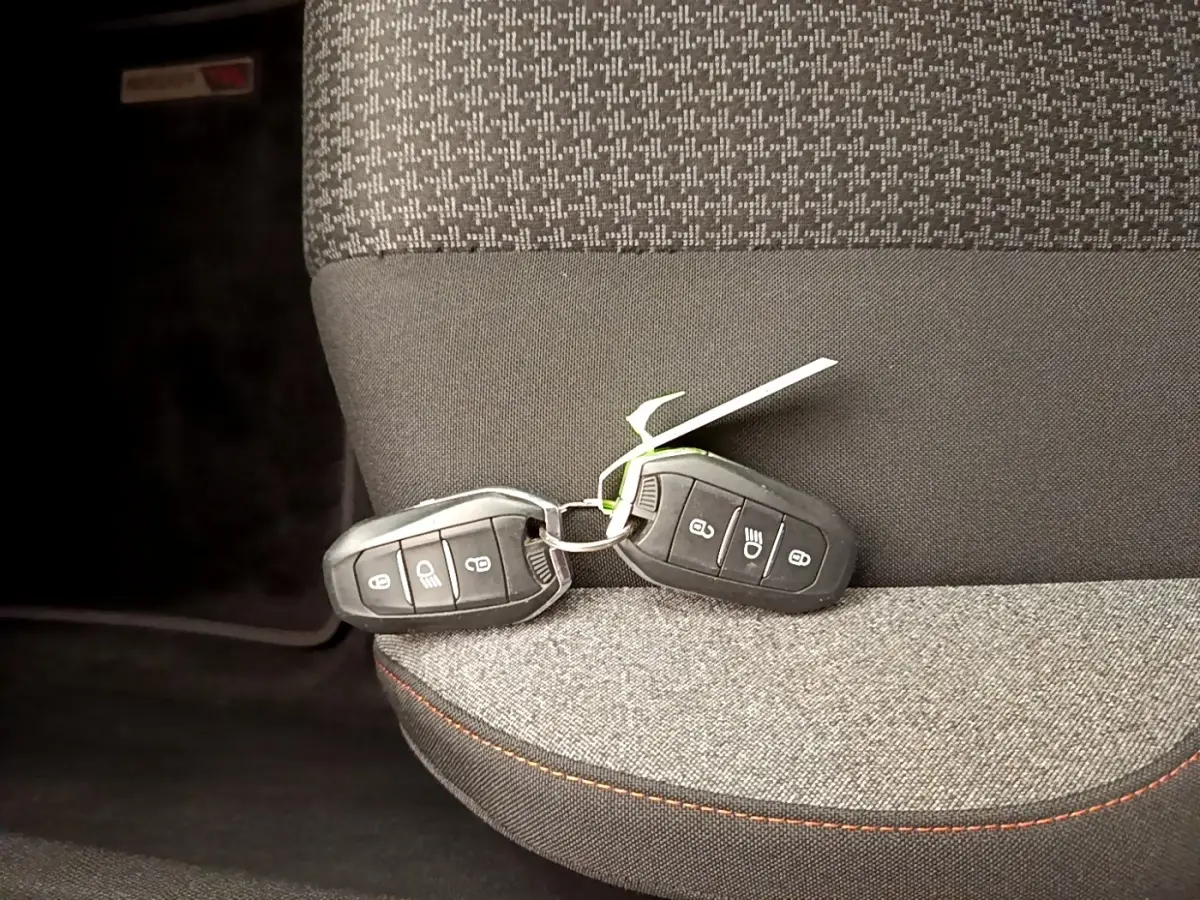 Gros plan sur deux clés de voiture noires posées sur un siège tissu gris à surpiqûres orange du Peugeot 5008.