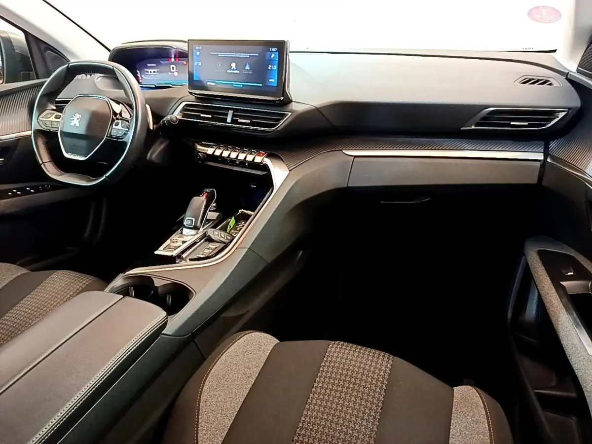 Intérieur Peugeot 5008 gris, vue côté passager avant, tableau de bord moderne avec écran tactile et volant compact cuir.
