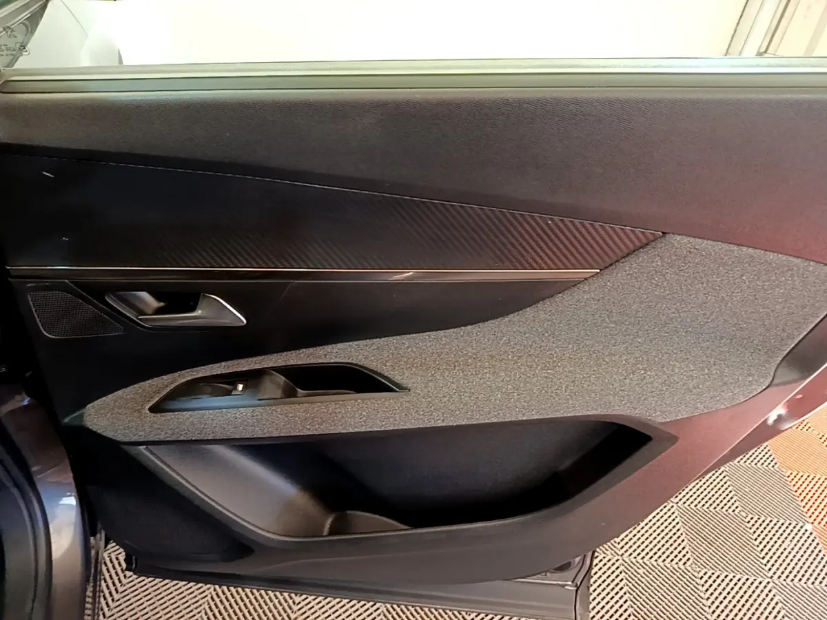 Vue intérieure côté gauche de la porte avant d’un Peugeot 5008 gris clair, avec habillage texturé et poignée argentée.