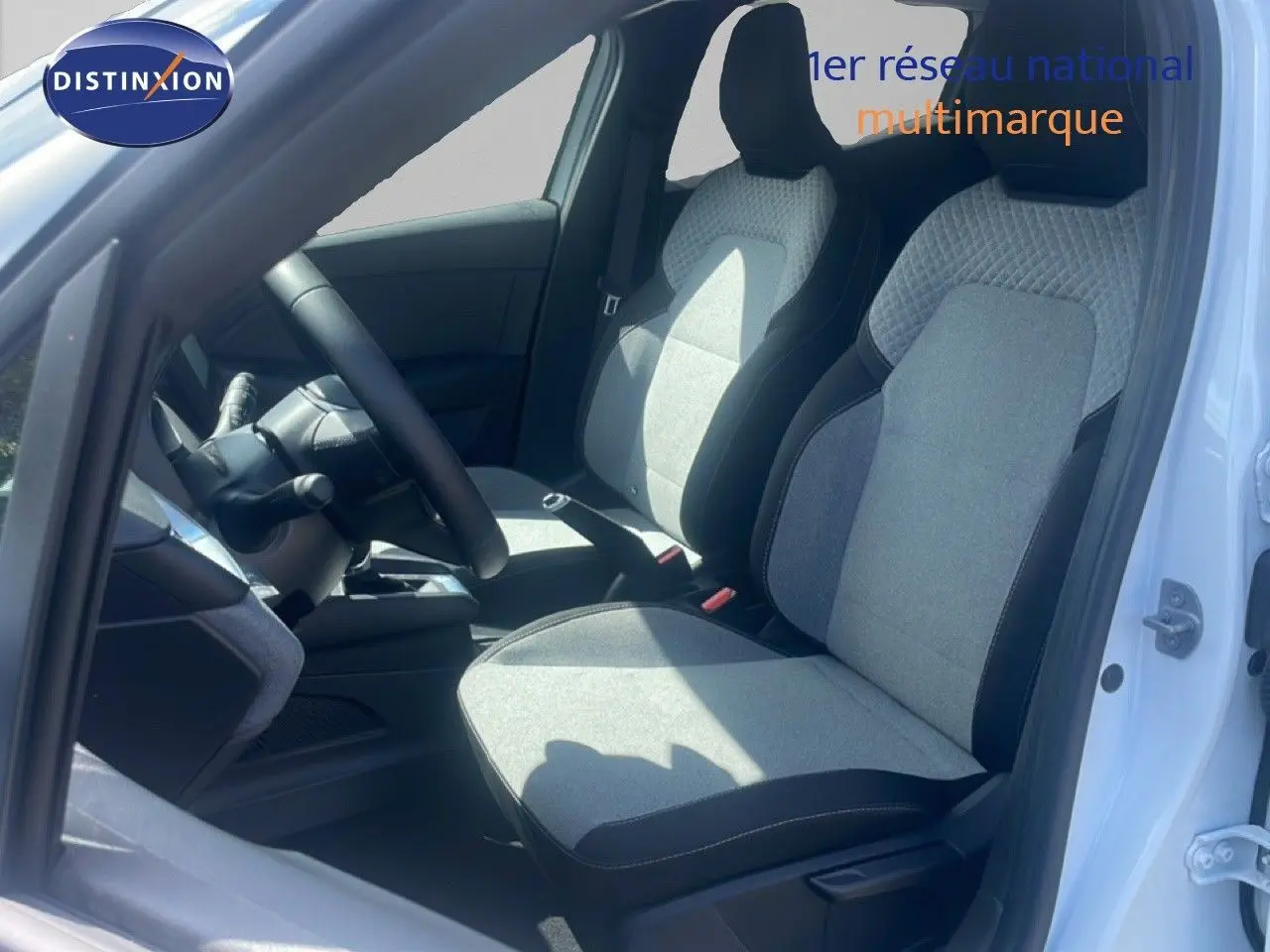 Vue intérieure côté conducteur de la Renault Clio blanche 2025, sièges tissu gris clair avec contours noirs.