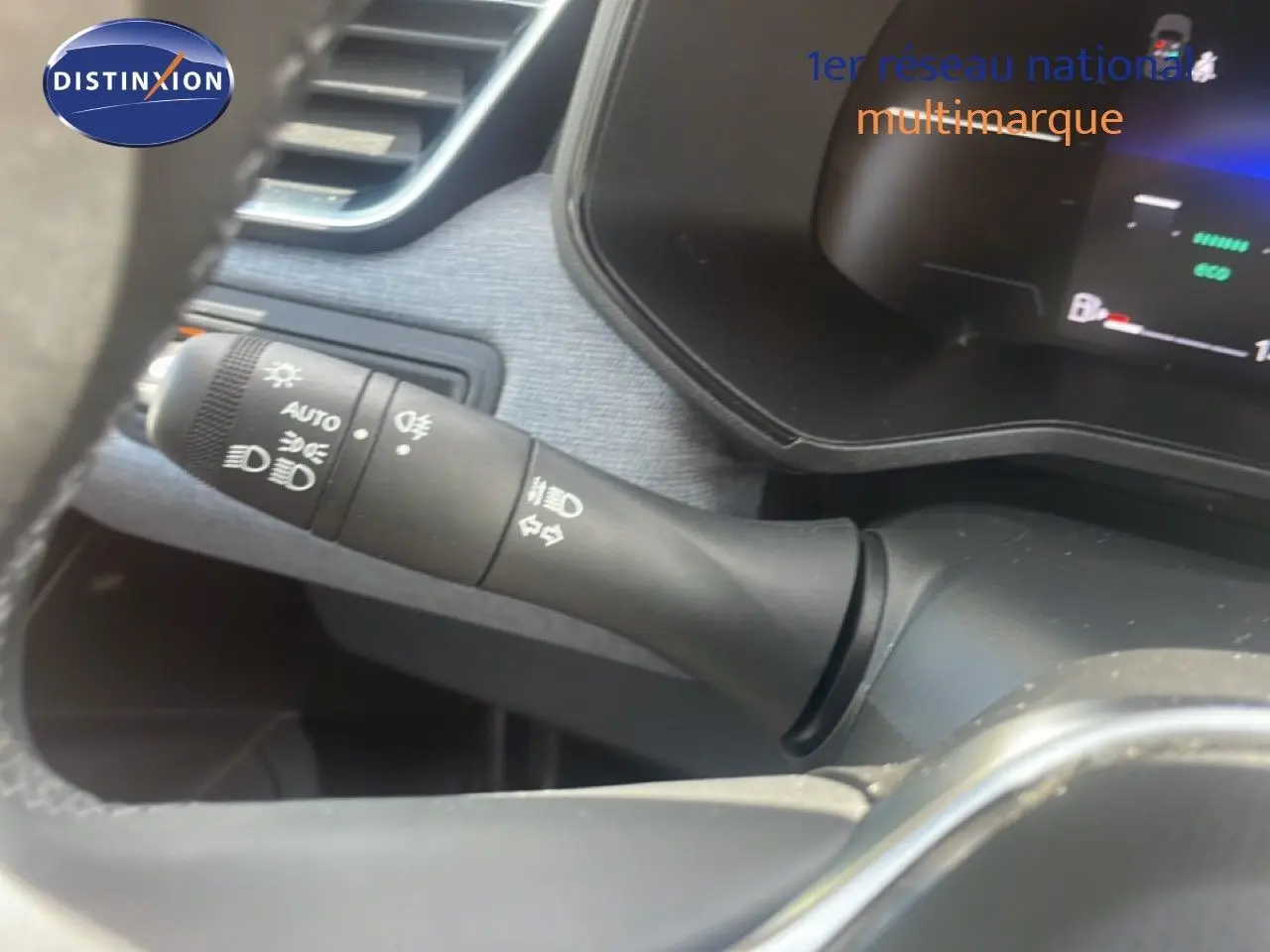 Gros plan sur la commande des feux et clignotants à gauche du volant dans l’habitacle d’une Renault Clio blanche.
