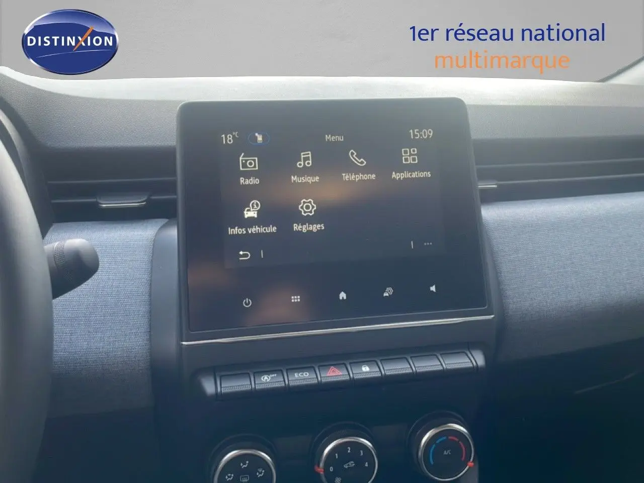 Vue intérieure centrée sur l’écran tactile du tableau de bord d’une Renault Clio blanche, avec commandes de climatisation visibles.