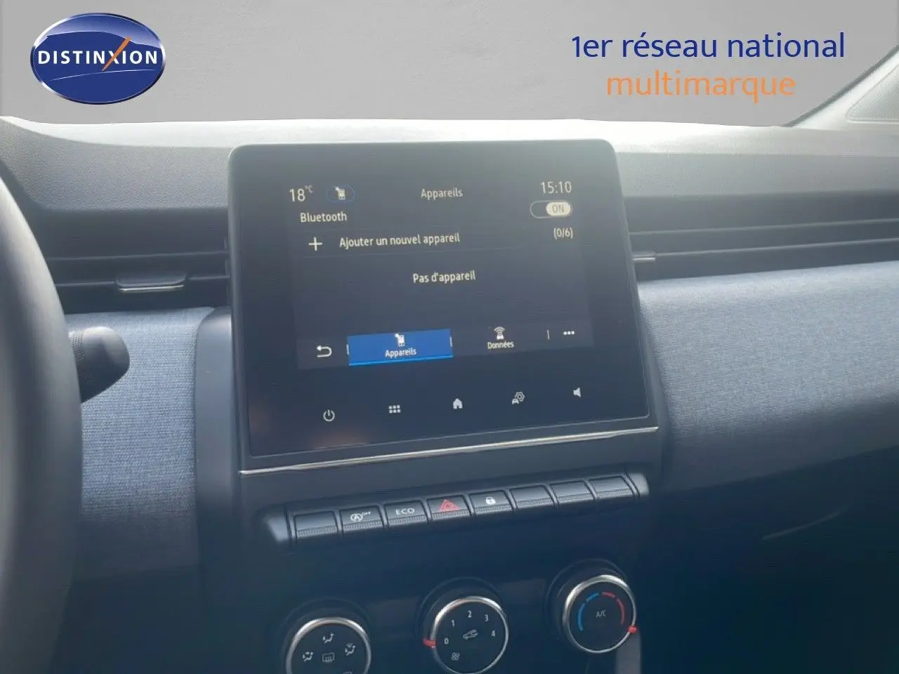 Vue intérieure centrée sur l'écran tactile et la console centrale d'une Renault Clio blanche, avec commandes climatisation visibles.