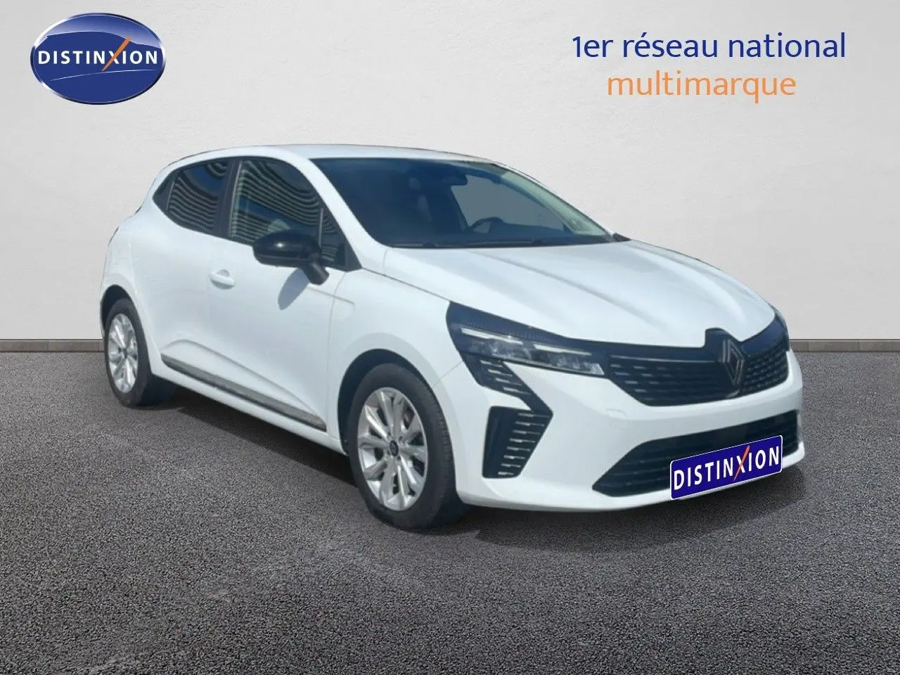 Renault Clio blanche vue 3/4 avant droit, avec calandre noire et jantes alliage argentées sur sol gris.