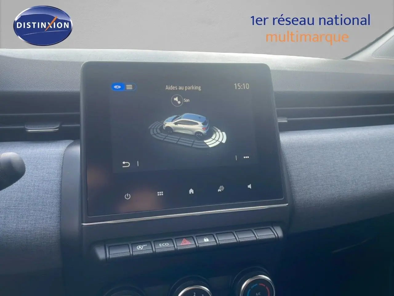 Écran tactile central de la Renault Clio blanche 2025 montrant l'aide au parking, avec tableau de bord gris et commandes en dessous.