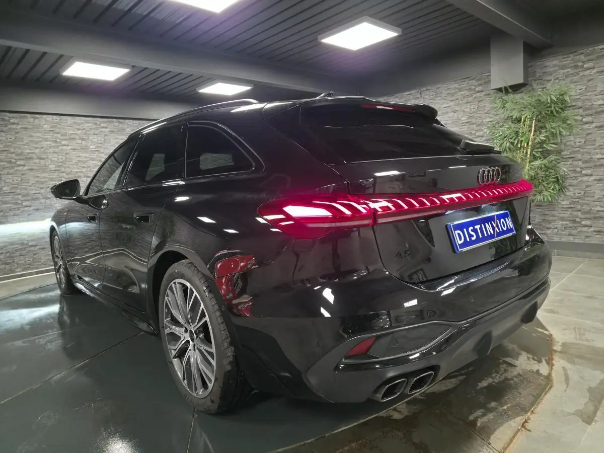Audi A5 Avant noir vue 3/4 arrière droit en intérieur, feux arrière LED allumés et jantes 19 pouces visibles.