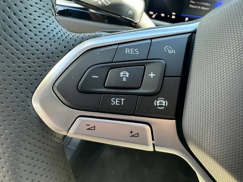 Gros plan sur les commandes de régulateur de vitesse au volant cuir perforé du Volkswagen T-Roc noir intense nacré 2025.