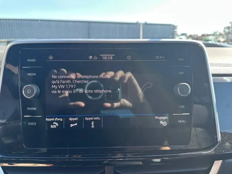 Écran tactile central du Volkswagen T-Roc 2025 affichant un message de connexion Bluetooth, reflet de mains visible.
