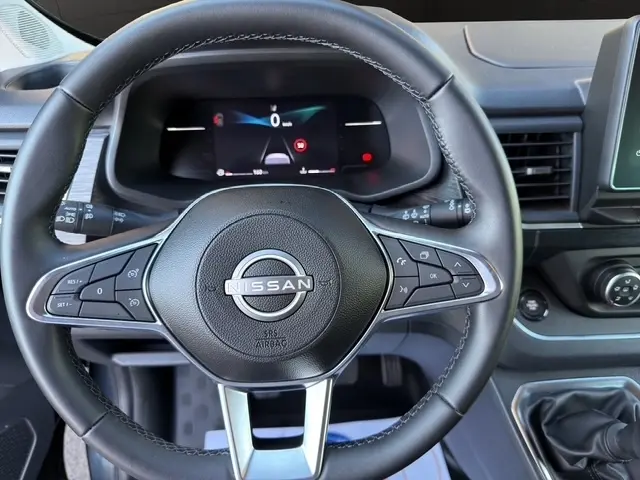 Vue rapprochée du volant en cuir noir du Nissan Primastar 2025 avec commandes multifonctions et tableau de bord numérique.