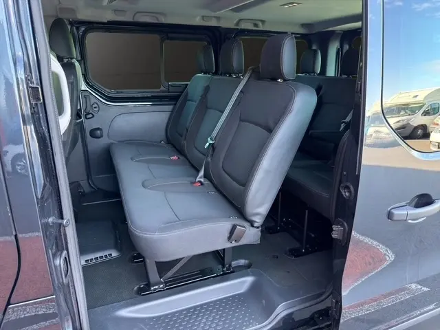 Vue latérale intérieure montrant les sièges arrière en tissu gris foncé du Nissan Primastar 2025 avec porte latérale ouverte.