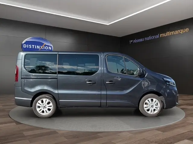 Vue de profil côté droit d’un Nissan Primastar gris foncé avec vitres teintées et jantes alliage en showroom.
