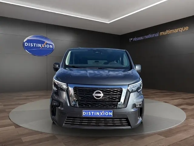 Vue de face d'un Nissan Primastar gris foncé avec calandre noire et logo Nissan bien visible, en showroom.