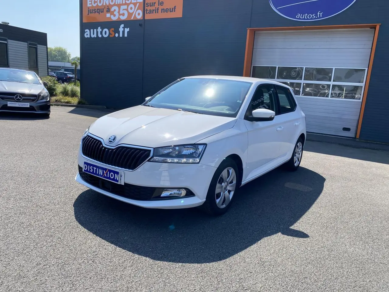 Vue 3/4 avant droite d'une Skoda Fabia blanche 2021 garée devant un bâtiment commercial.
