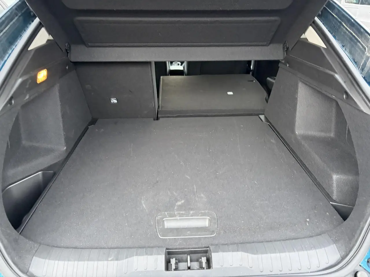 Coffre ouvert d’un Renault Arkana bleu Zanzibar, vue arrière montrant la banquette arrière partiellement rabattue.