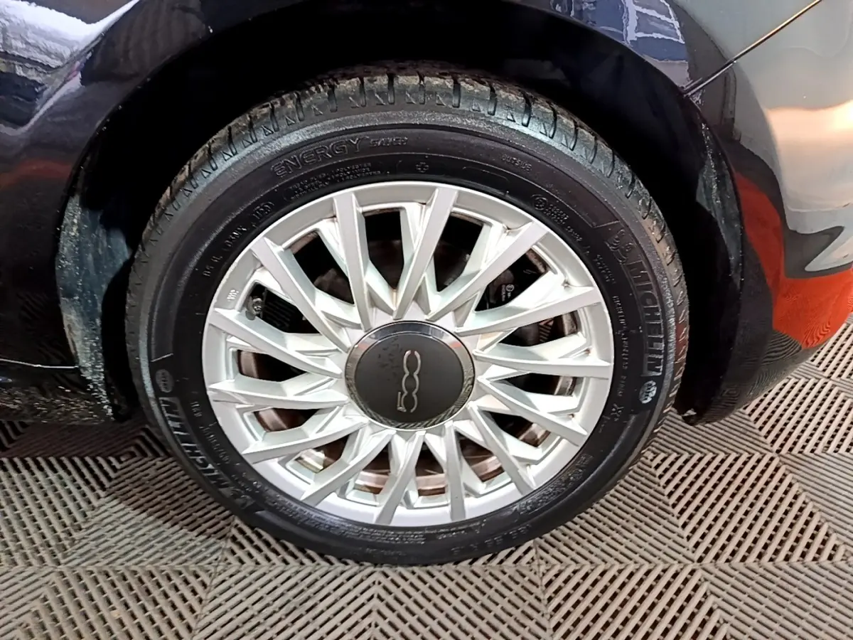 Gros plan sur la roue avant gauche d'une FIAT 500 noire, mettant en valeur la jante argentée au design fin et élégant.