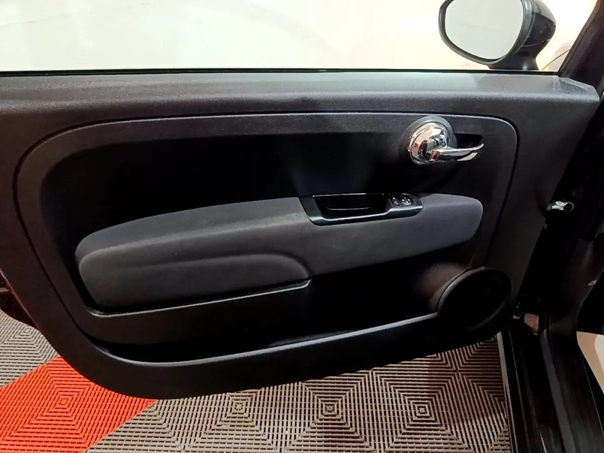 Vue rapprochée de la porte intérieure côté conducteur noire de la FIAT 500 Lounge 2019 avec poignée chromée et commandes de vitres.