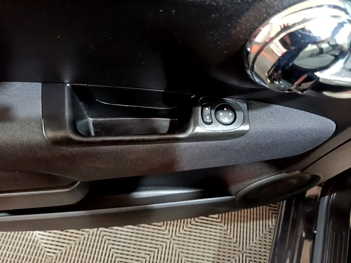 Gros plan sur la poignée intérieure et les commandes de réglage des rétroviseurs côté conducteur d'une Fiat 500 noire.