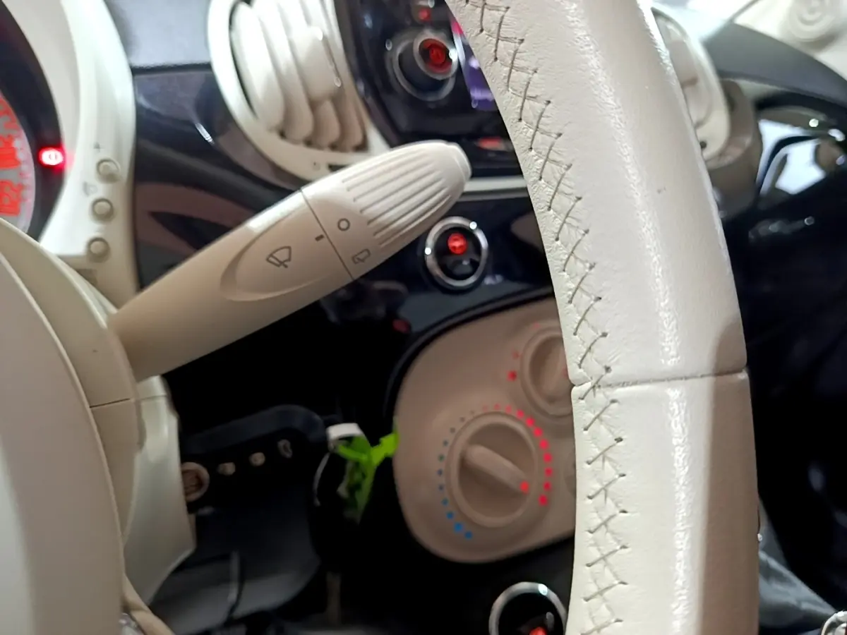 Gros plan sur le volant cuir beige et la commande d’essuie-glace de la Fiat 500 noire, tableau de bord en arrière-plan.