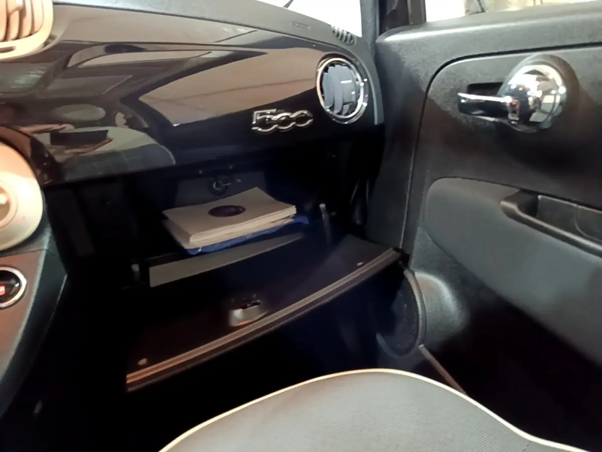 Vue intérieure côté passager de la Fiat 500 noire, montrant la boîte à gants ouverte et le tableau de bord brillant.