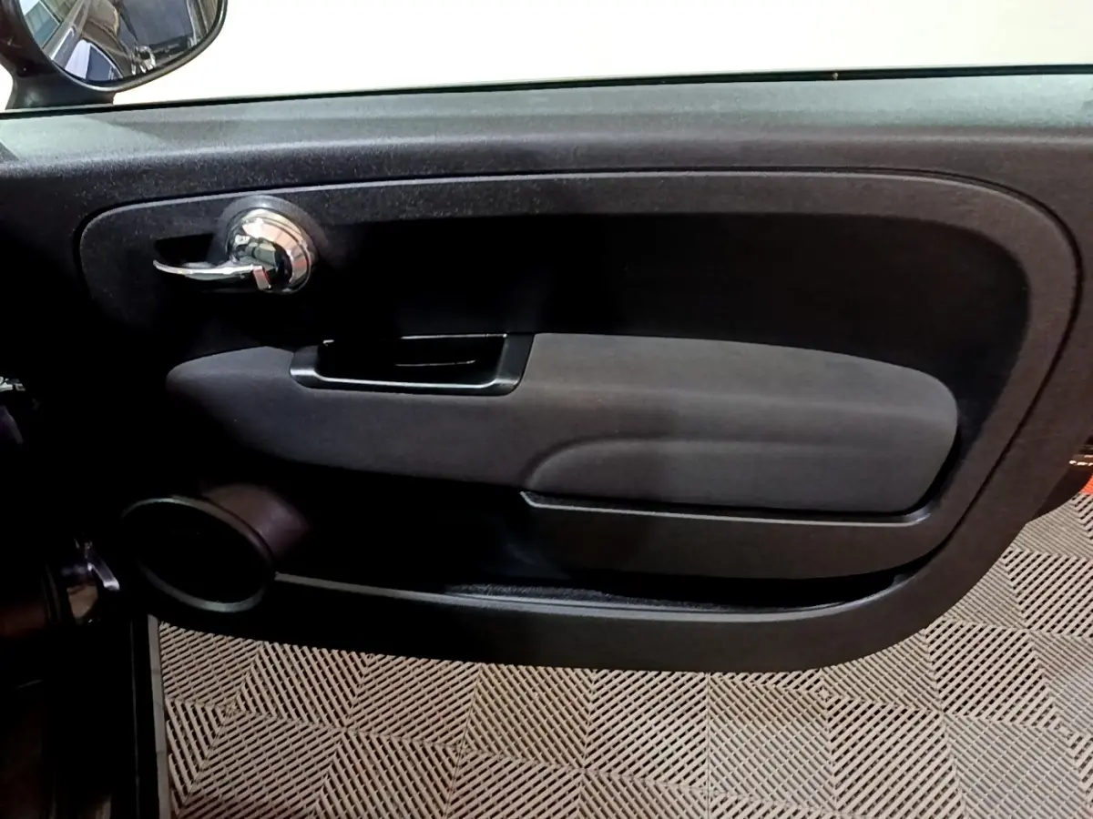 Vue rapprochée de la porte côté conducteur noire de la Fiat 500 Lounge avec poignée chrome et haut-parleur intégré.