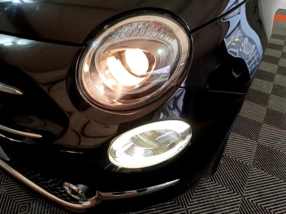 Gros plan sur le phare avant droit allumé d'une Fiat 500 noire, mettant en valeur ses feux LED et détails chromés.