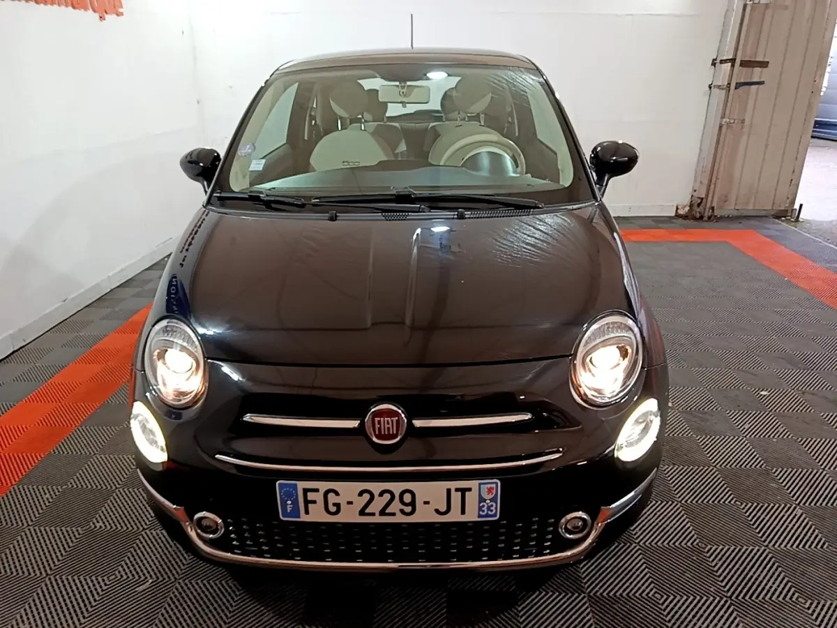 Vue avant d'une FIAT 500 noire de 2019 avec phares allumés dans un garage intérieur.