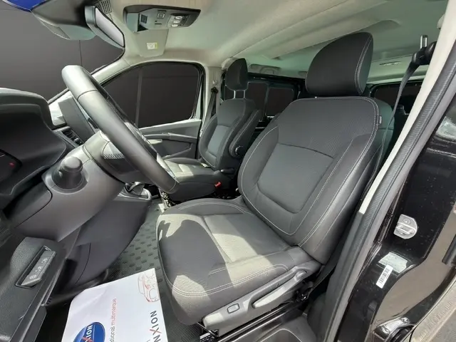 Vue intérieure côté conducteur du Nissan Primastar noir 2025, mettant en valeur les sièges avant en tissu et le volant multifonction.