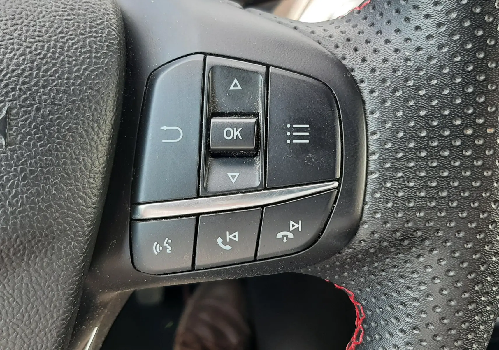 Gros plan sur les commandes multifonctions du volant perforé avec surpiqûres rouges du Ford Puma blanc 2022.