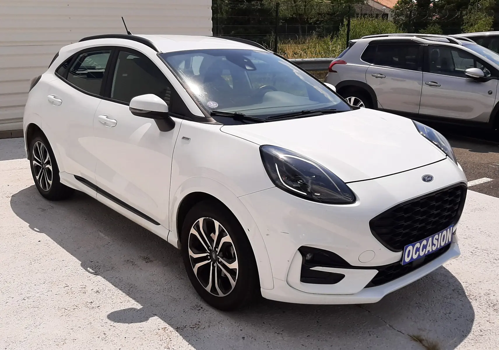Ford Puma blanc en 3/4 avant droit, avec calandre noire et jantes alliage bicolores, stationné en extérieur.