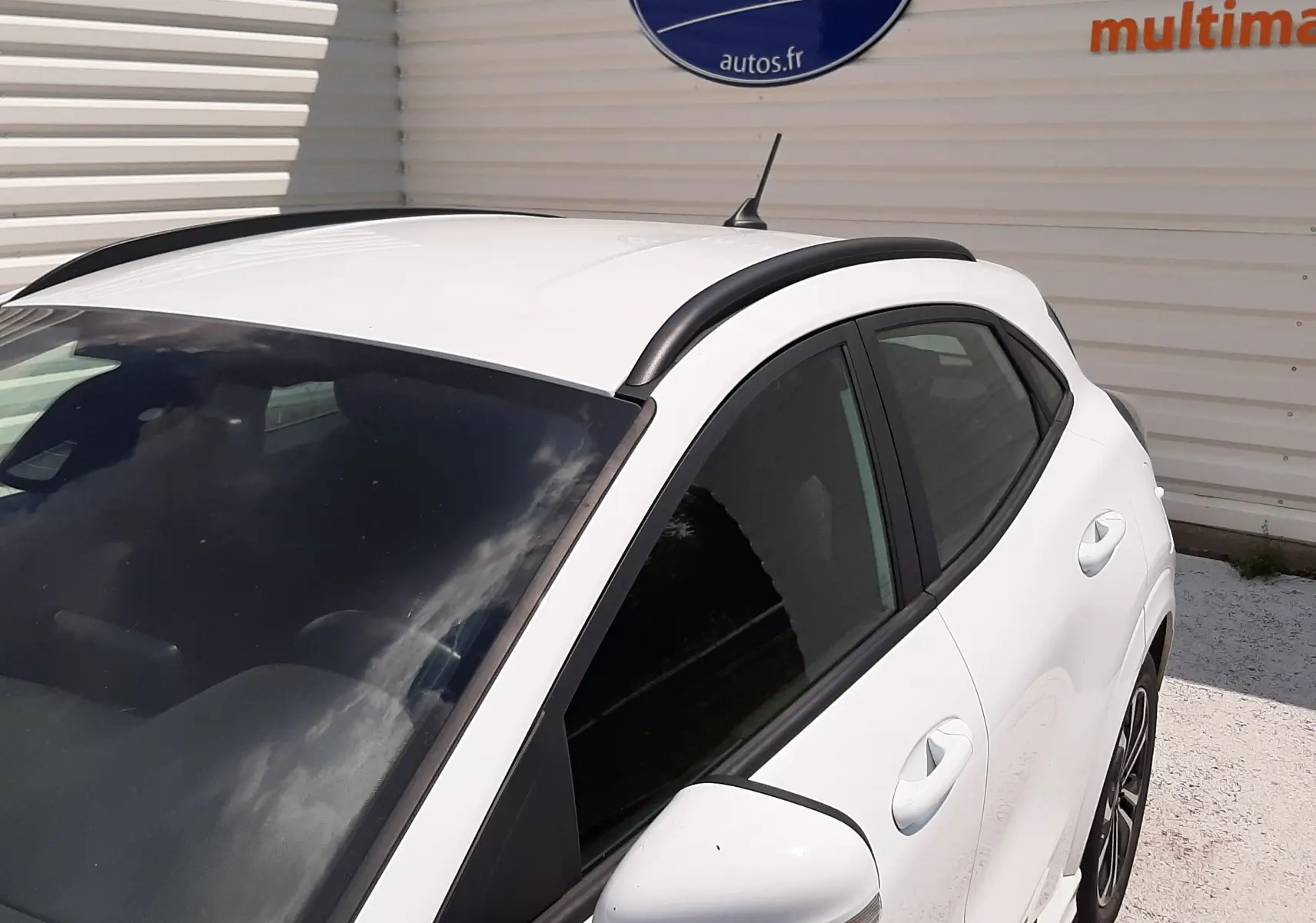 Vue 3/4 avant droit du Ford Puma blanc 2022 ST-LINE avec barres de toit noires et vitres teintées.