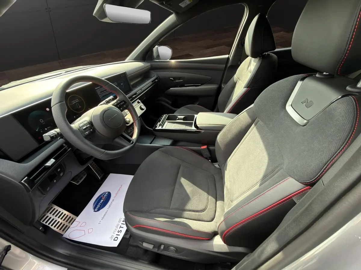 Vue intérieure côté conducteur du Hyundai Tucson 1.6 Hybrid N Line gris clair, sièges sport avec surpiqûres rouges et tableau de bord numérique.