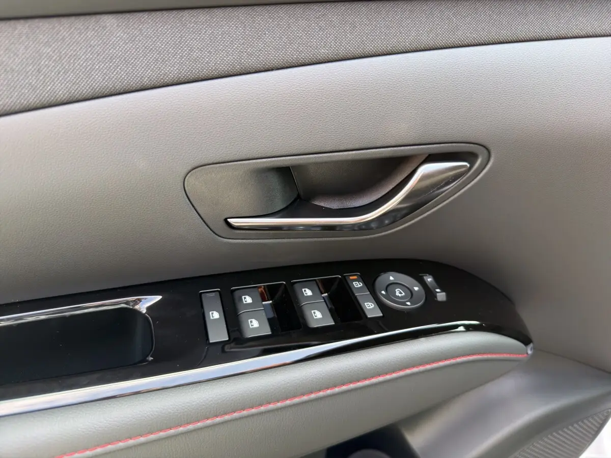 Gros plan sur la poignée de porte intérieure gris clair et les commandes électriques des vitres du Hyundai Tucson 1.6 Hybrid N Line 2026.