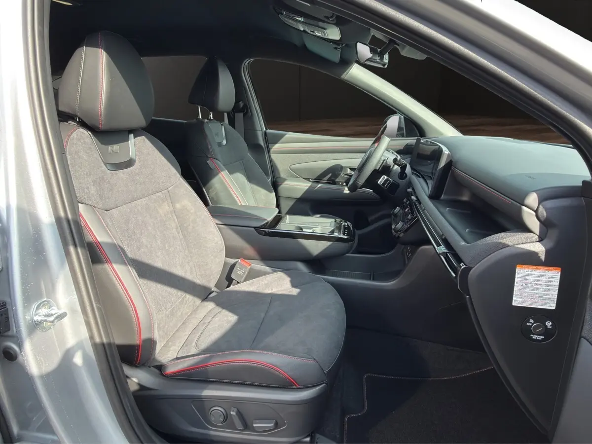 Vue intérieure côté conducteur du Hyundai Tucson 1.6 Hybrid N Line gris clair, sièges sport avec surpiqûres rouges et tableau de bord moderne.