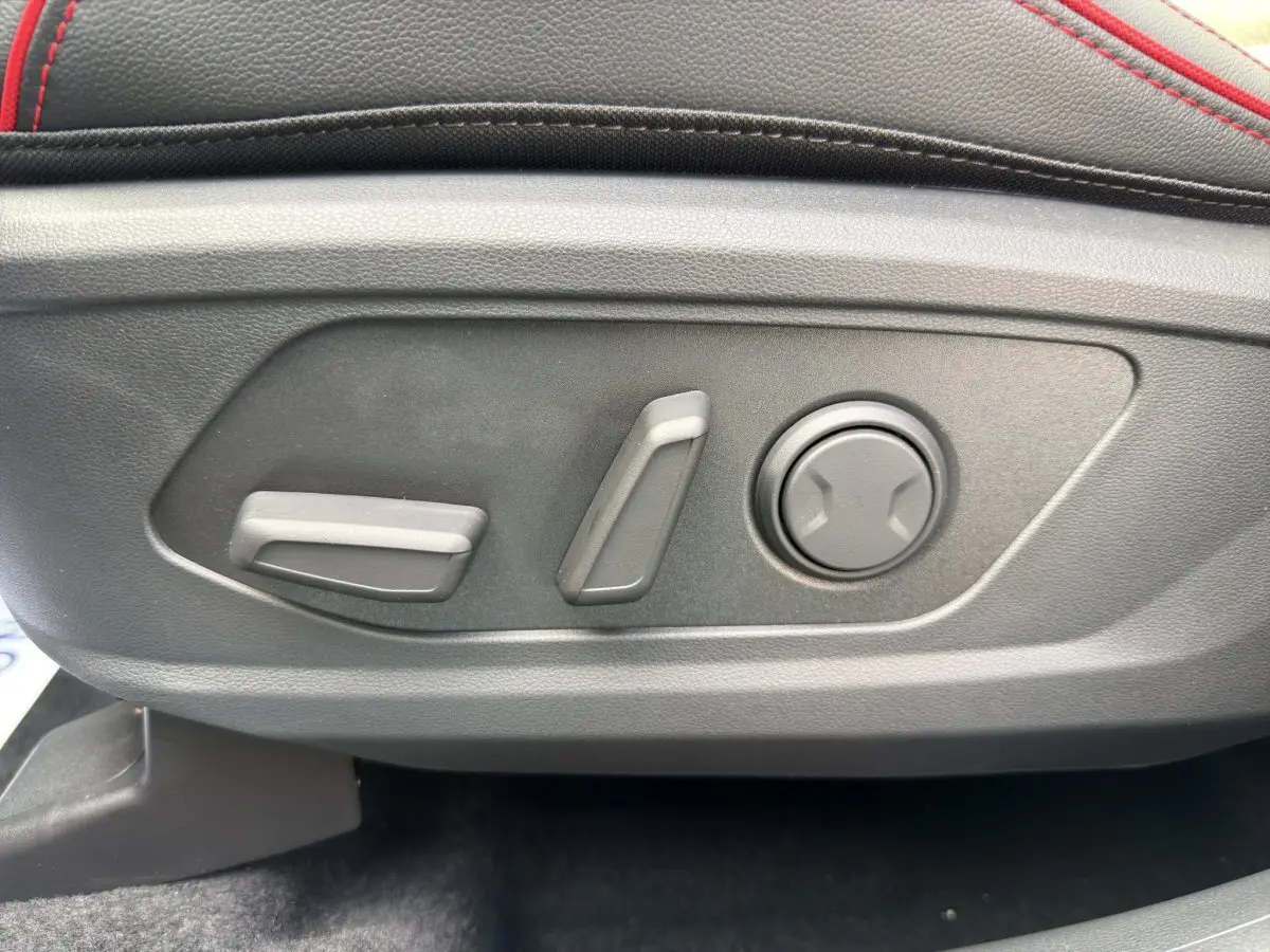 Détail des commandes de réglage électrique du siège avant avec surpiqûres rouges sur cuir noir du Hyundai Tucson 1.6 Hybrid 2026.
