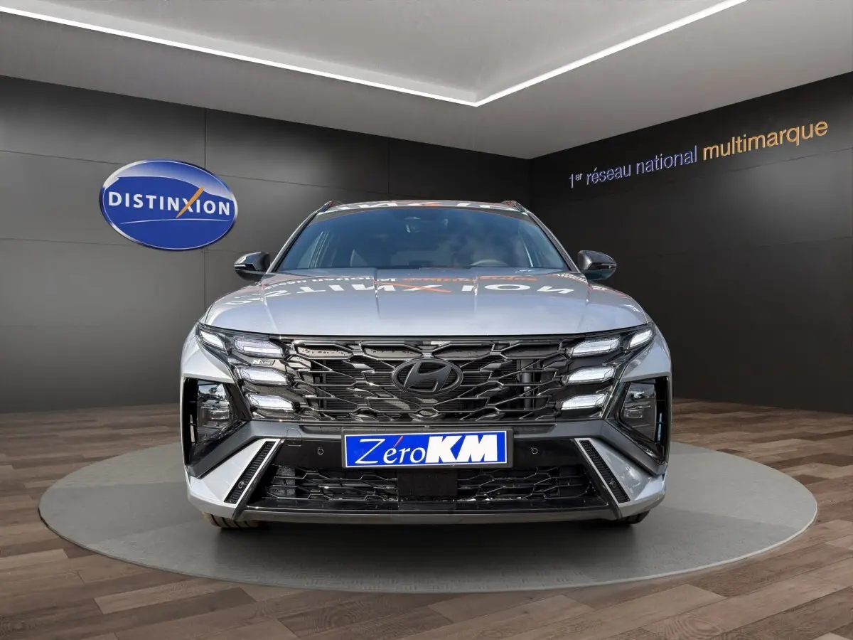 Vue frontale d'un Hyundai Tucson gris clair 2026 avec calandre noire et éclairage LED distinctif en showroom.