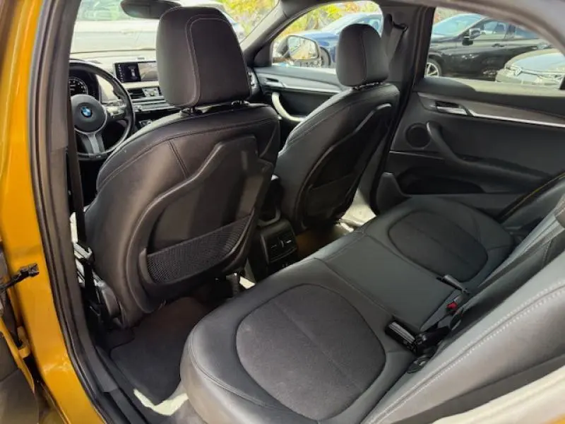 Vue intérieure arrière droite du BMW X2 Galvanic Gold, sièges noirs en cuir et tableau de bord visible à l'avant.