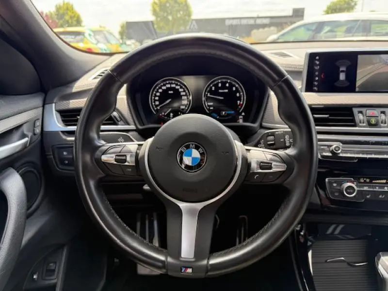 Vue centrée sur le volant M Sport noir du BMW X2 hybride, avec tableau de bord et écran multimédia visibles.